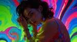 The camera captures a striking brunette in a luxurious satin gown, her silhouette illuminated by viv