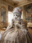 A humanoid Ragdoll cat dressed in a baroque-style dress, drinking tea. It is wearing a silver wig li